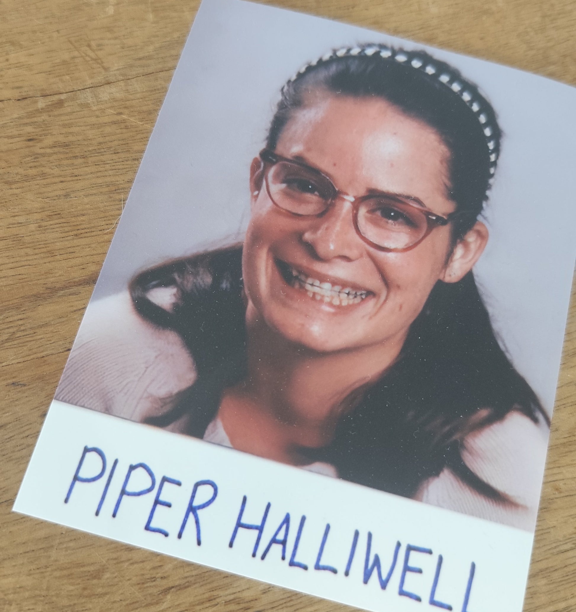 Card with a photo of Piper Halliwell and her name on a wooden surface